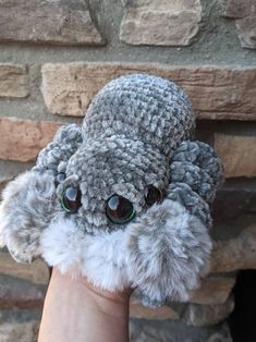 a hand holding a stuffed animal in front of a brick wall with eyes on it