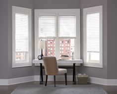 a chair sitting in front of two windows next to a table with a lamp on it