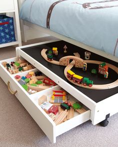 a child's bedroom with toy train tracks and toys in the drawer under the bed