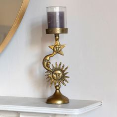 a candle holder with a gold sun and moon decoration on top of a white mantle