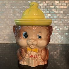 a ceramic cat figurine with a yellow hat on it's head sitting on a counter