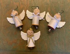 four little angel ornaments with bells on top of a wooden table next to each other