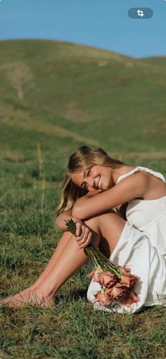 a woman sitting in the grass with her hands on her knees, holding a flower