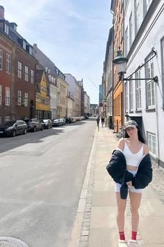 a woman standing on the side of a street next to tall buildings and wearing short shorts