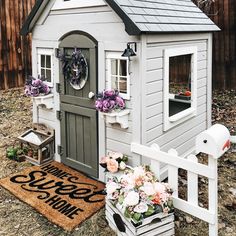 a white dog house with flowers and wreaths on the front door, next to a welcome mat