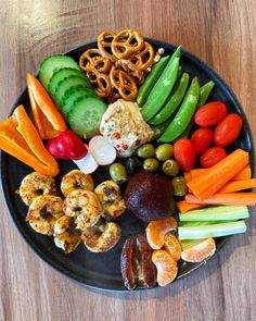 a black plate topped with lots of different types of vegetables and fruits next to pretzels