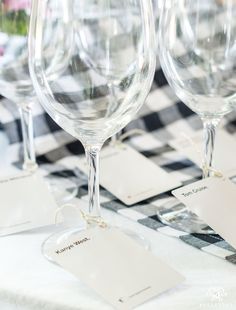 empty wine glasses sitting on top of a checkered table cloth with tags attached to them