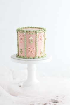 a pink and green cake sitting on top of a white cake platter with ribbons