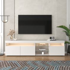 a flat screen tv sitting on top of a white entertainment center next to a potted plant