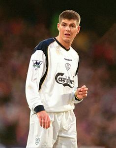 a young man in white soccer uniform standing on the field with his hands clasped to his chest