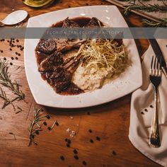 a white plate topped with meat covered in gravy next to a fork and knife