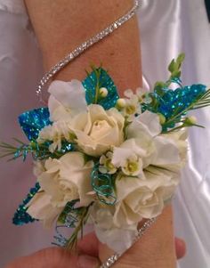 a bride's wrist is adorned with white flowers and blue sequined accents