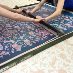 two people are cutting fabric with scissors on a tablecloth covered in blue and pink designs