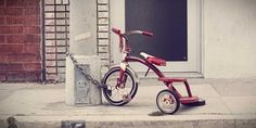 a red tricycle is parked on the sidewalk