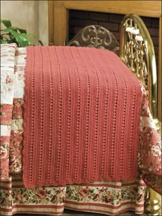 a red blanket sitting on top of a bed next to a chair