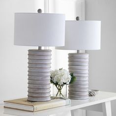 two lamps sitting on top of a table next to a book and vase with flowers