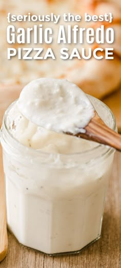 a jar filled with white sauce sitting on top of a wooden table next to pizza