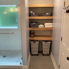 a walk in shower sitting next to a white door with baskets on the bottom shelf