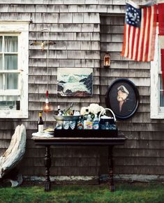 a table with bottles and glasses on it in front of a house next to an american flag