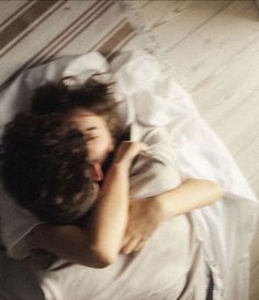 a young man laying on top of a bed next to a wooden floor covered in white sheets