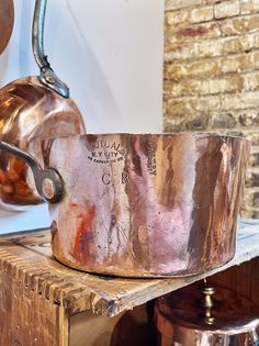 an old copper pan sitting on top of a wooden table next to a brick wall