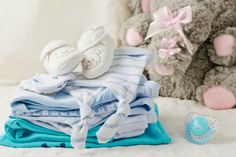 a pile of baby clothes sitting next to a teddy bear