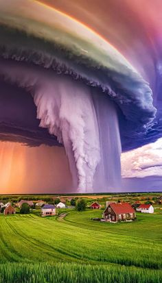 a large storm is coming in the sky over a green field with houses and trees