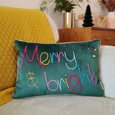 a merry and bright pillow sitting on top of a white couch next to a yellow throw pillow