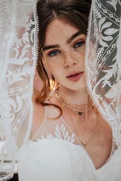 a woman with freckled hair wearing a white dress and gold necklace under a veil