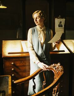 a woman standing in front of a desk holding a piece of paper