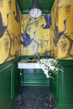 a bathroom with yellow and green wallpaper has a white sink in the corner next to it