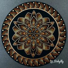 an intricately painted circular design on a black surface with gold and white dots in the center