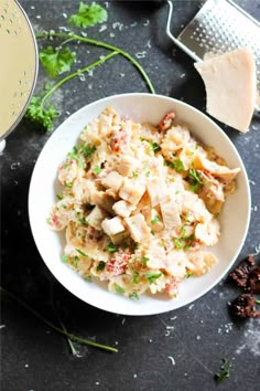 a white bowl filled with chicken salad next to cheese and parsley on the side