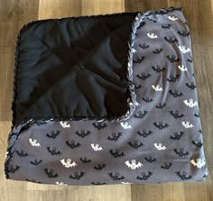 a black and white bat print blanket laying on top of a wooden floor next to a pillow