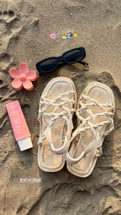 a pair of sandals, sunglasses and hair clip laying in the sand next to a tube of sunscreen