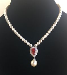 Classic Red Ruby cubic zirconia teardrop and pearls bridal necklace in rhodium plated brass setting.  This gorgeous necklace features a large teardrop pendant with pear cut red cubic zirconia center surrounded by tiny round zirconia crystals with a dangling 12mm Austrian crystal pearl drop. This pendant is strung in a row of 6mm Austrian crystal pearls. Length of the necklace is 16 inches and comes with 2 inches adjustable extender and closed with a lobster clasp. Necklace is also available with Formal Red Pearl Drop Jewelry, Red Pearl Necklace With Pearl Drop, Red Teardrop Necklace For Wedding, Elegant Red Pearl Necklace For Weddings, Elegant Red Pear-shaped Necklace, Elegant Red Drop Necklace, Elegant Red Pearl Necklace For Formal Occasions, Elegant Red Teardrop Pendant Drop Necklace, Formal Teardrop Pearl Bridal Necklace