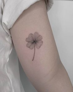 a small four leaf clover tattoo on the left inner arm, with a single flower in the center