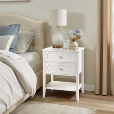 a white nightstand sitting on top of a bed next to a window