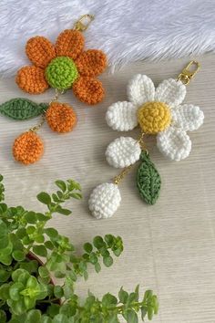 three crocheted flowers hanging from hooks on a table next to a potted plant