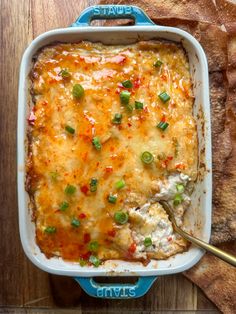 a casserole dish with meat and vegetables in it on a wooden table next to bread