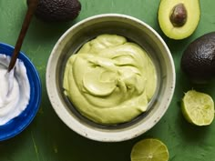 an avocado dip in a bowl next to sliced limes and other fruit