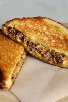 two grilled cheeseburger sandwiches cut in half on top of a piece of wax paper