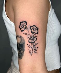 a woman's arm with a skull and flowers tattoo on the left upper arm