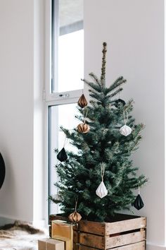 a small christmas tree in a wooden crate with ornaments hanging from it's sides