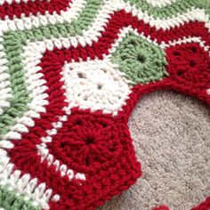 a red and green crocheted rug on the floor with a white circle in the middle