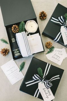 three black and white boxes with christmas cards in them next to pinecone cones