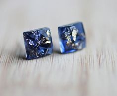 two square shaped blue and gold earrings sitting on top of a wooden table