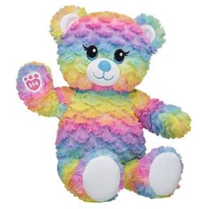 a multicolored teddy bear sitting on top of a white surface with its paw up