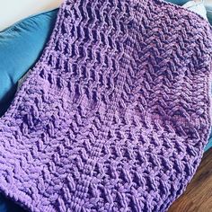 a purple crocheted blanket sitting on top of a blue couch