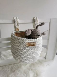 a small crocheted basket with two stuffed animals in it sitting on a white chair